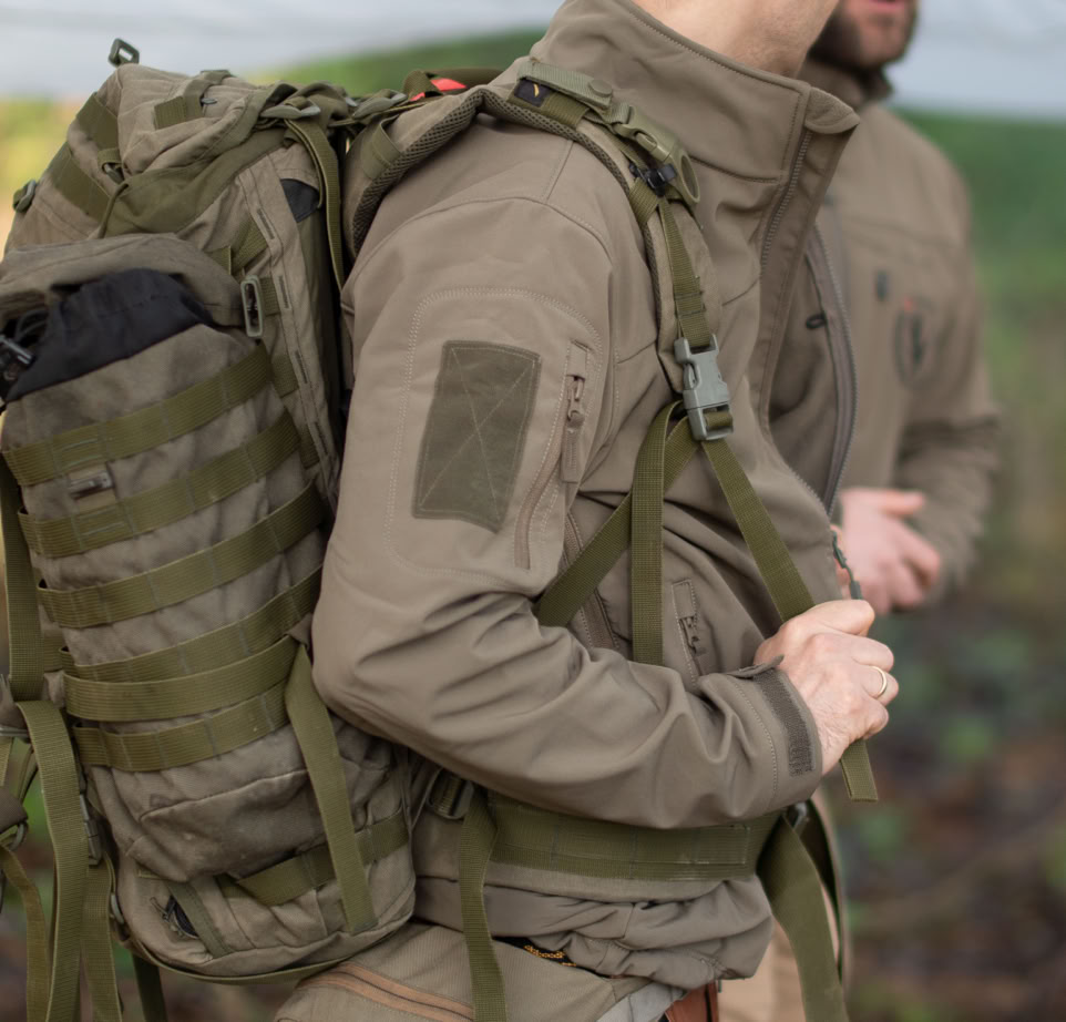 A man handling a portable camping stove near a tent in a grassy outdoor area.